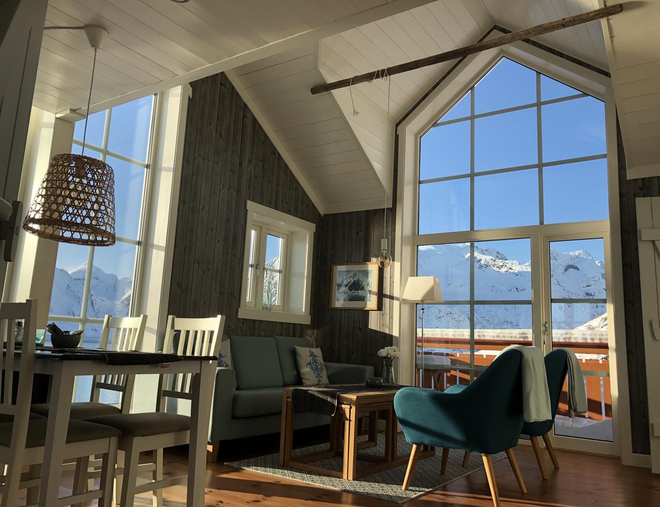 Stue med to store og et lite vindu mot fjorden. En turkis sofa, to turkise lenestoler og et bord.