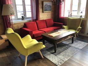 Stue med gamle trevegger. En r&oslash;d sofa, et bord og to limegule lenestoler.