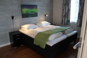 Soverom med to enkeltsenger satt sammen, den ene kan heves og senkes. Gr&aring; vegg med en nordlysbilde, hvite laken og et gr&oslash;nt sengeteppe.