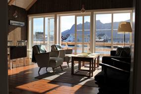 Stue med store vinduer store vinduer med utsikt over Hamn&oslash;y havn. En sofa, et bord og to lenestoler.