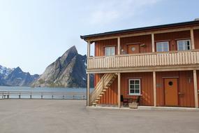 Oransje leilighets bygg i to etasjer. Reinefjorden og fjellet Olstind i bakgrunnen.