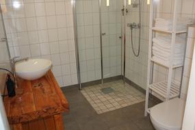 Bad med dusj- skyved&oslash;rer i glass, toalett montert p&aring; vegg, hylle for oppbevaring og benk med servant og speil p&aring; vegg