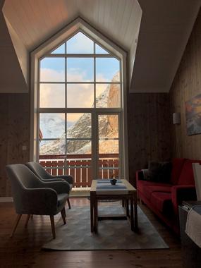 Vegg-til-tak vindu med sofa, bord og lenestoler fremfor hvor man kan slappe av og nyte utsikten over Reinefjorden. Lampetter p&aring; veggen over sofa 