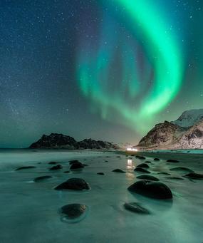 Gr&oslash;nt og bl&aring;tt nordlys over en strand i Lofoten