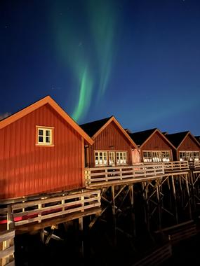 Gr&oslash;nt nordlys over 4 r&oslash;de rorbuer p&aring; Reinefjorden Sj&oslash;hus