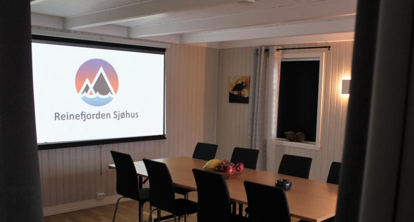 Foto fra m&oslash;terommet i V&aelig;reierg&aring;rden. 8 stoler og m&oslash;tebord og prosjektor-lerret p&aring; veggen